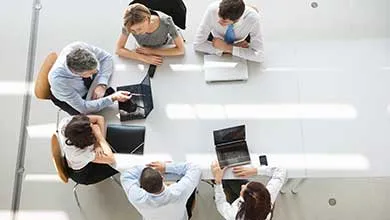 Overhead view: Six professionals with laptops at a white conference table