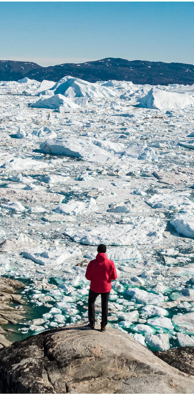Travel in arctic landscape nature with icebergs - Greenland tourist man explorer - tourist person looking at amazing view of Greenland icefjord - aerial drone image. Man by ice and iceberg, Ilulissat.